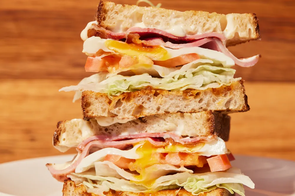 A stacked egg, ham, cheese and tomato sandwich on toasted sourdough