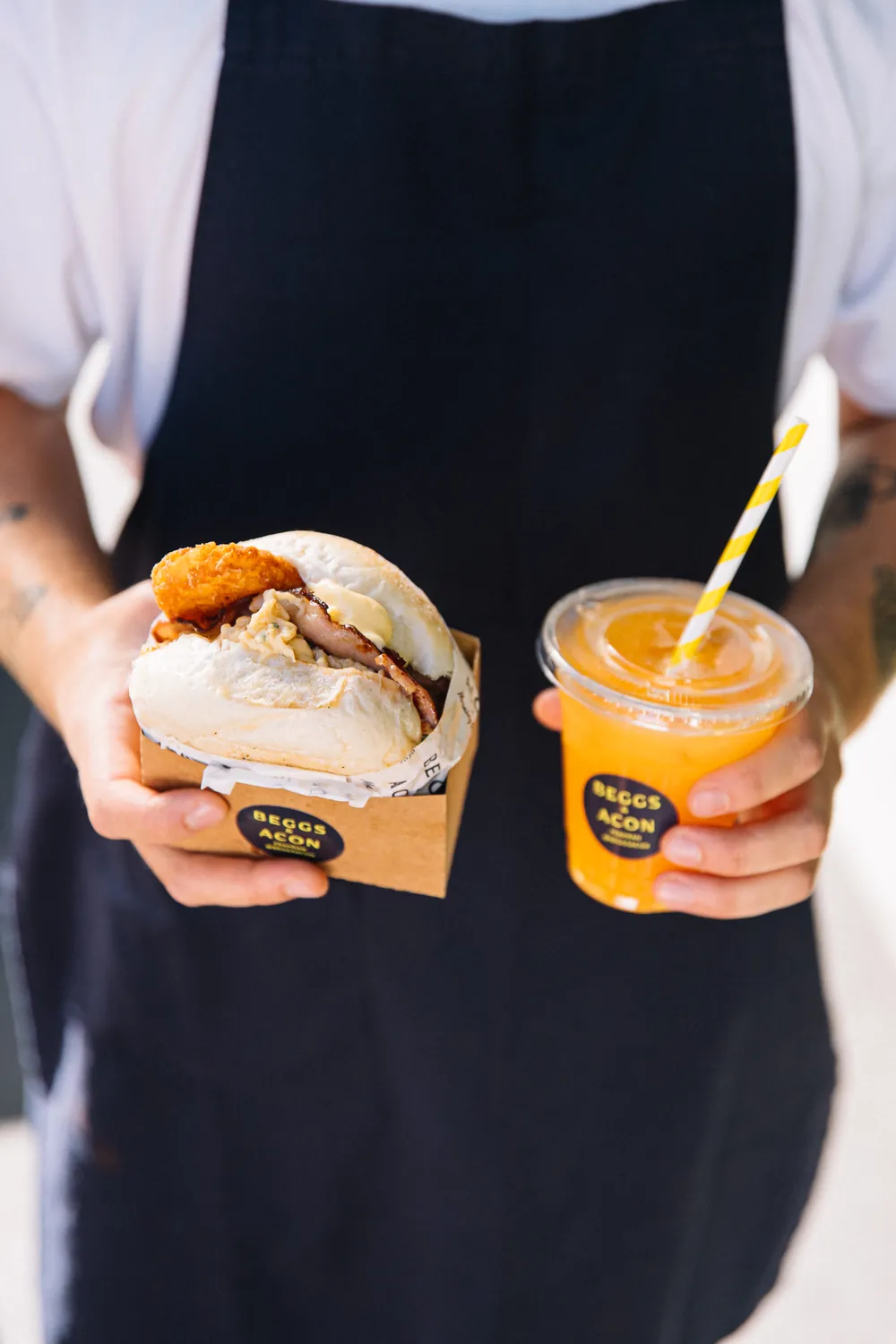 An egg and bacon roll and a fresh orange juice in Beggs & Acon branded packaging